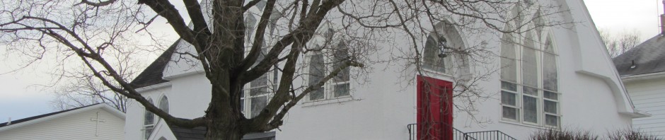 A white church with a large tree and red banners in winter.