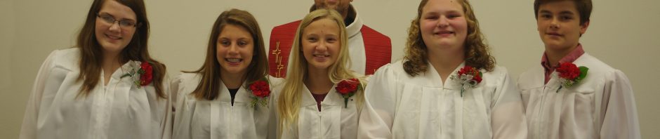 A group of young choir members in white robes posing for a photo indoors.