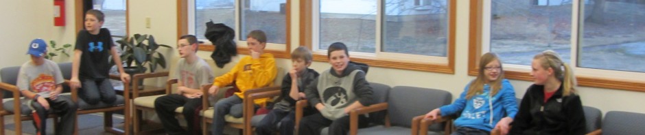 A group of people sitting on chairs in a room with large windows and colorful artwork.