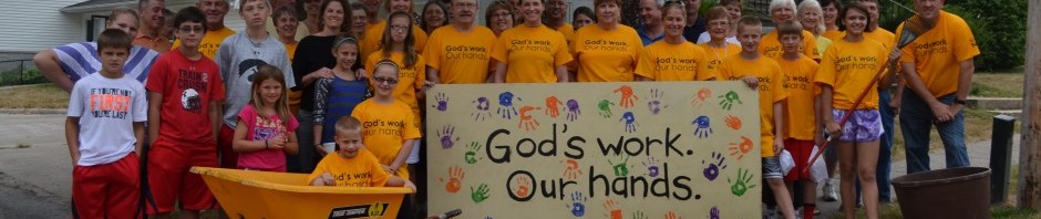 Group of people in yellow shirts holding a sign with colorful handprints.