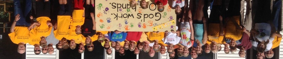 Group of people holding a colorful banner with handprints and text.