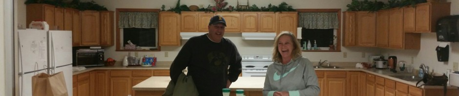 Two people standing behind a kitchen counter with food items.