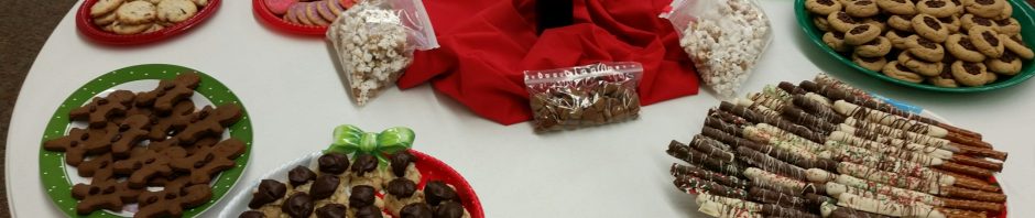 Assorted cookies and treats arranged on a table with a red centerpiece and flowers.