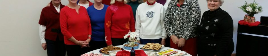 A group of older women standing behind a table with various cookies.