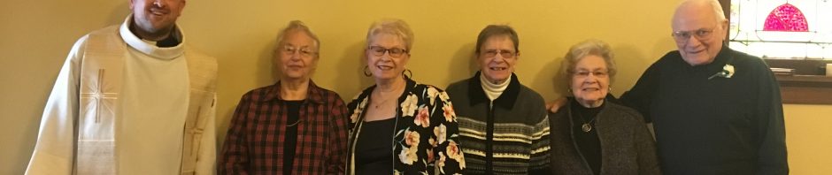 A group of six people posing indoors against a yellow wall.