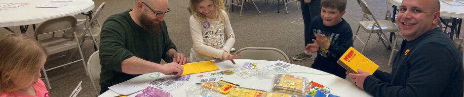 Adults and a child create crafts at a round table with colorful materials.
