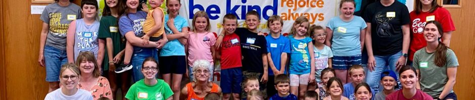 A diverse group of children and adults posing in a colorful room with positive words on the wall.