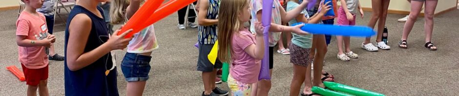 Children playing with colorful balloon swords indoors.