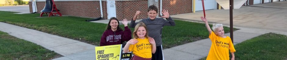 Kids holding signs and wearing yellow shirts outside a building.