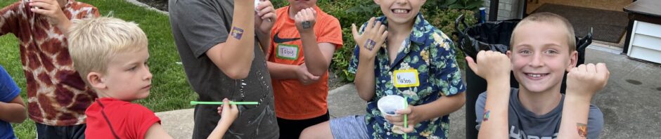 Five boys enjoying snacks outdoors by a white fence.