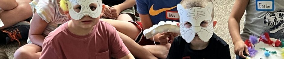 Children sitting on the ground wearing handmade animal masks.