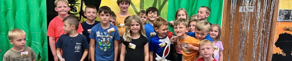 A group of children smiling in front of a colorful backdrop with balloons.