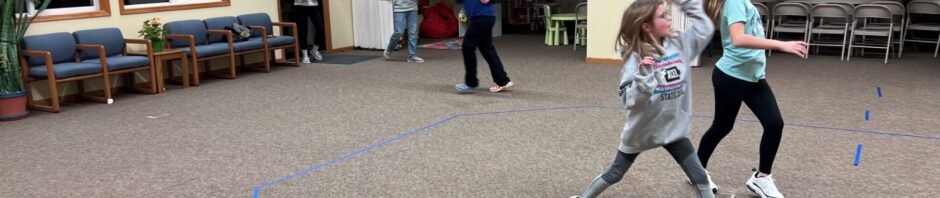 Children playing and running inside a large room with marked floor.