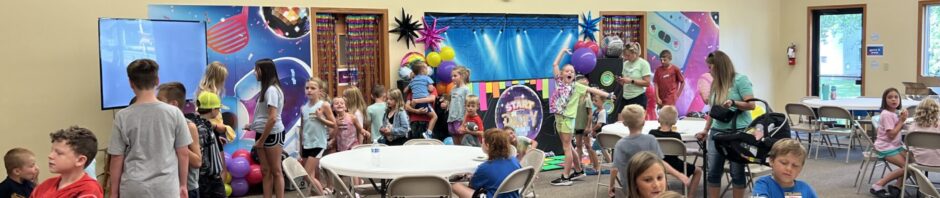 A lively church hall event with children and adults gathered around tables.