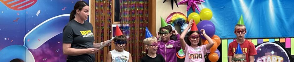 Children enjoying a colorful party with balloons and costumes on stage.