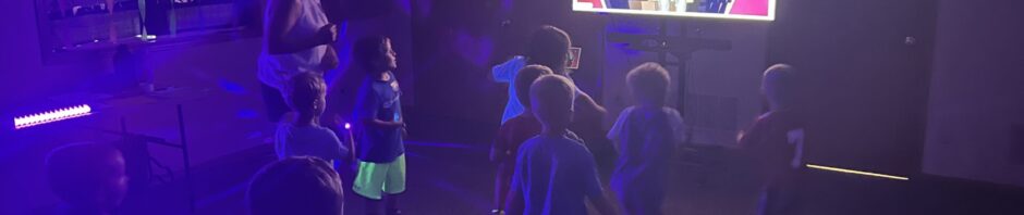 Children playing in a dimly lit room with a colorful screen.