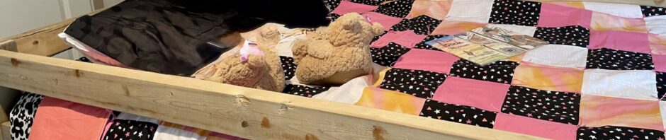 Two dogs resting on a colorful quilt inside a wooden bed frame.