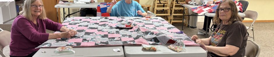 Group of women assembling quilt pieces at tables in a cozy room.
